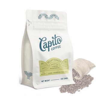 A white package of Capito Coffee's Decaf Blend is labeled as organic decaf coffee and small-batch roasted in Boston, Massachusetts using the Swiss water process. The label highlights flavors of caramel, marshmallow, and cocoa. A burlap sack with coffee beans is partially visible next to the bag. Net weight: 12oz (340g).